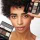 Black model with curly hair and light sking holding two powder kits