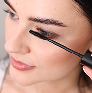 Fair skinned model applying the mascara seen from the side