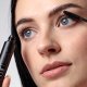 Model with blue eyes applying the mascara seen from below