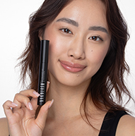 Asian model holding the mascara up to her cheek