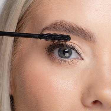 Model smiling while applying Nanolash mascara